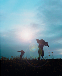 Zwei Silhouetten laufen auf einem Feld auf die strahlende Sonne zu.