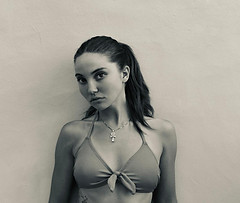 Young woman in bikini top and white pants poses in front of wall