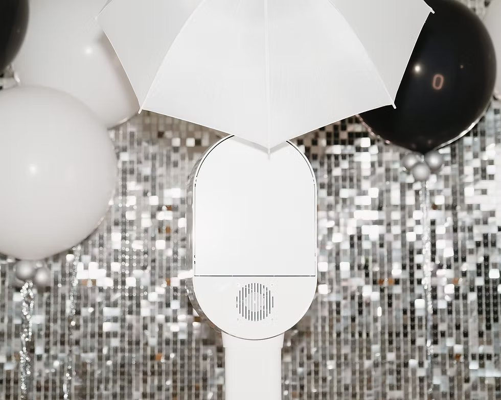 White photo booth with umbrella, surrounded by black and white balloons with a silver sequin backdrop, creating a festive atmosphere.