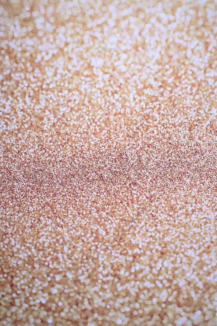 Close-up of sparkling rose gold glitter creating a shimmering and festive texture. No people or text present. Bright and cheerful mood.