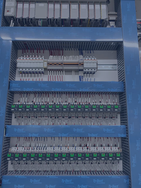 A close up view of a sub panel outside of al electrical cabinet with control relays, din rail, wire duct and fuses mounted on the surface of the metal sub panel.
