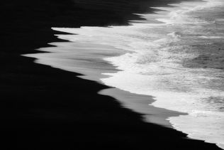 White Sea foam on dark volcanic beach. 