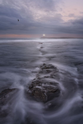 Lighthouse on Fuerteventura in stormy conditions with foamy waves in foreground.