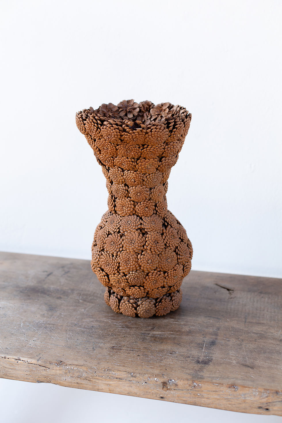 A collection of folk art vessels made from hand-stitched pine cones, formed into a vase, bowl and basket.