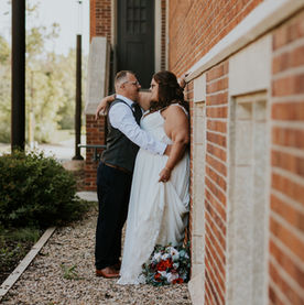 A couple leaning romantically against a brick heritage building in their wedding attire having a private intimate moment