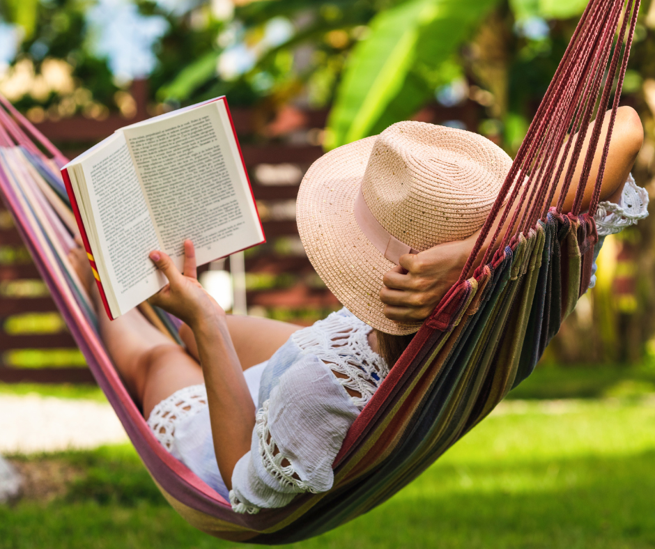 A person in a straw hat reads a book while relaxing in a colorful hammock. The setting is a lush, sunny garden, evoking tranquility.
