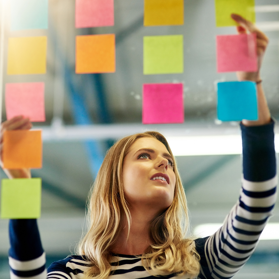 Woman in striped shirt places colorful sticky notes on glass in an office. Bright and focused atmosphere with blurred ceiling beams.