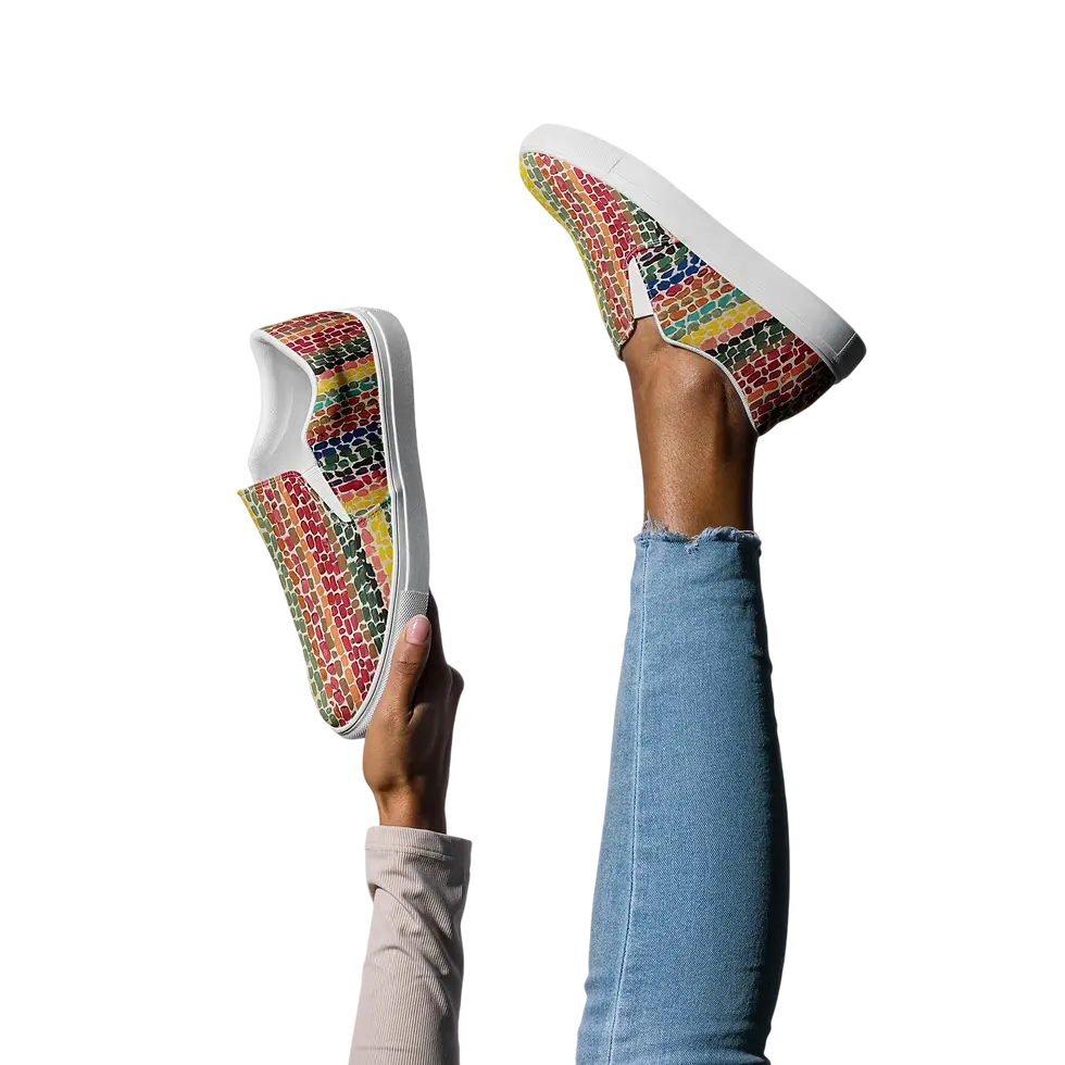 Studio photography of a pair of colorful, woven pattern slip-on shoes displayed against a stark black background. One shoe is worn on a leg while the other is held up, creating a playful and dynamic composition.