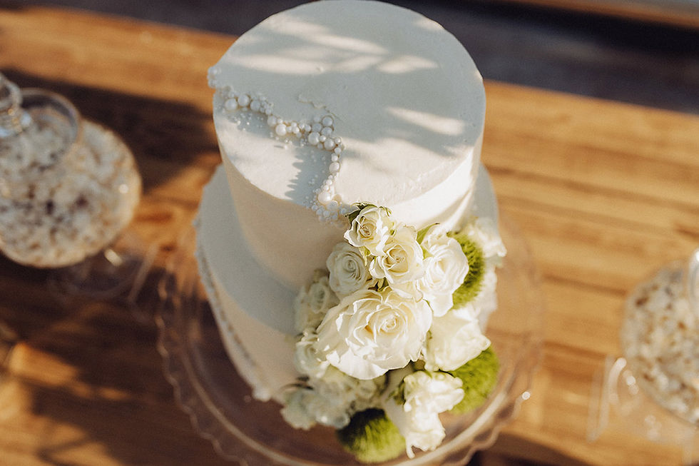 Bolo de casamento branco de dois andares com flores brancas, apontamentos verdes e detalhes delicados em pérolas.