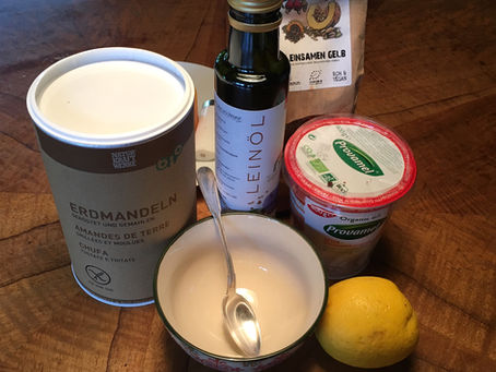 Holztisch mit Leinöl im Dunkelglas, Erdmandeln, einer Zitrone, gelben Leinsamen, veganem Quark von Provamel.