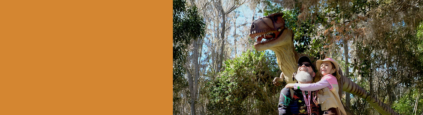 A young girl and her father smiling and looking at a T-Rex
