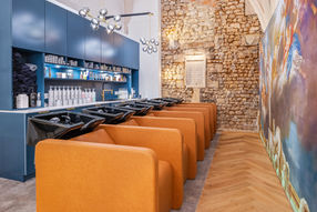Intérieur de salon de coiffure moderne avec stations de lavage, fauteuils en cuir orange, et fresque colorée.
