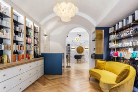 Salon de beauté moderne avec étagères de produits, canapé jaune et comptoir de réception en marbre.