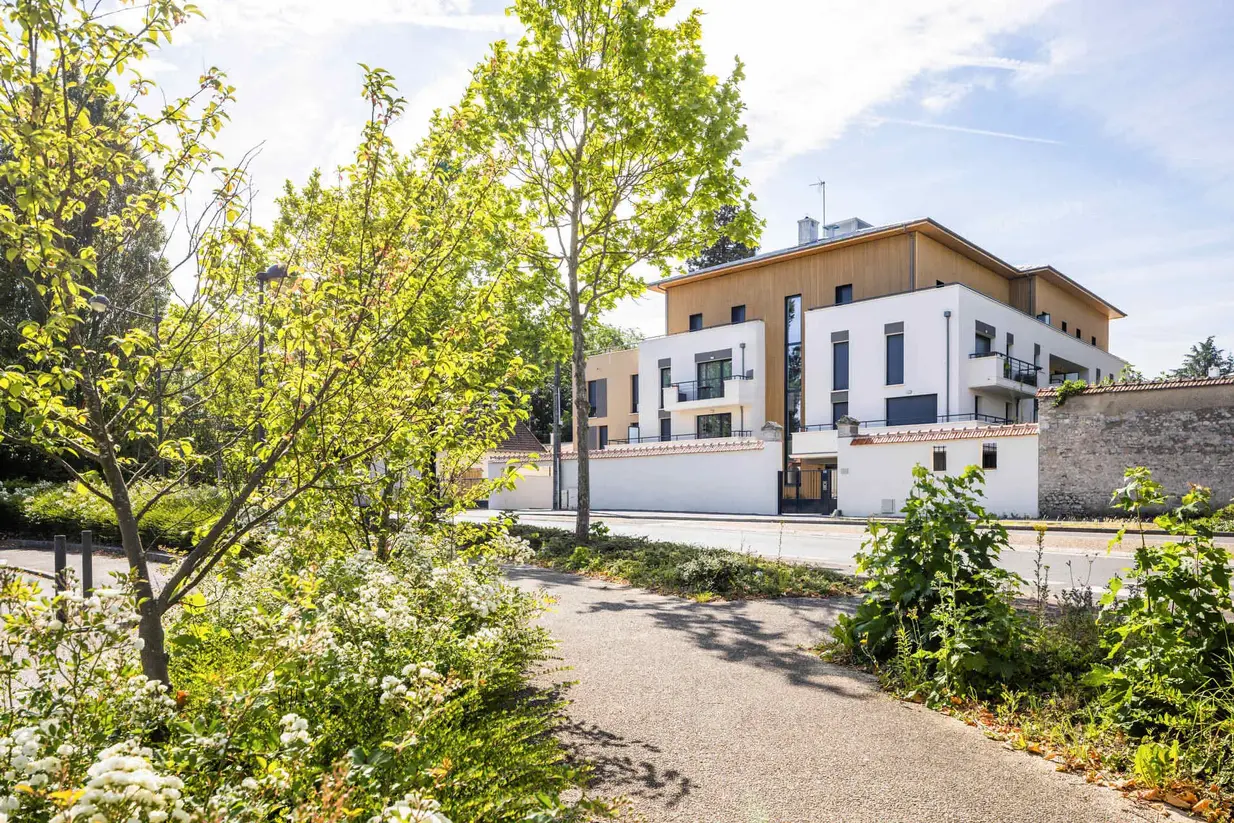 Photo d'un immeuble issue d'un programme immobilier avec vue sur la rue et des arbres. 