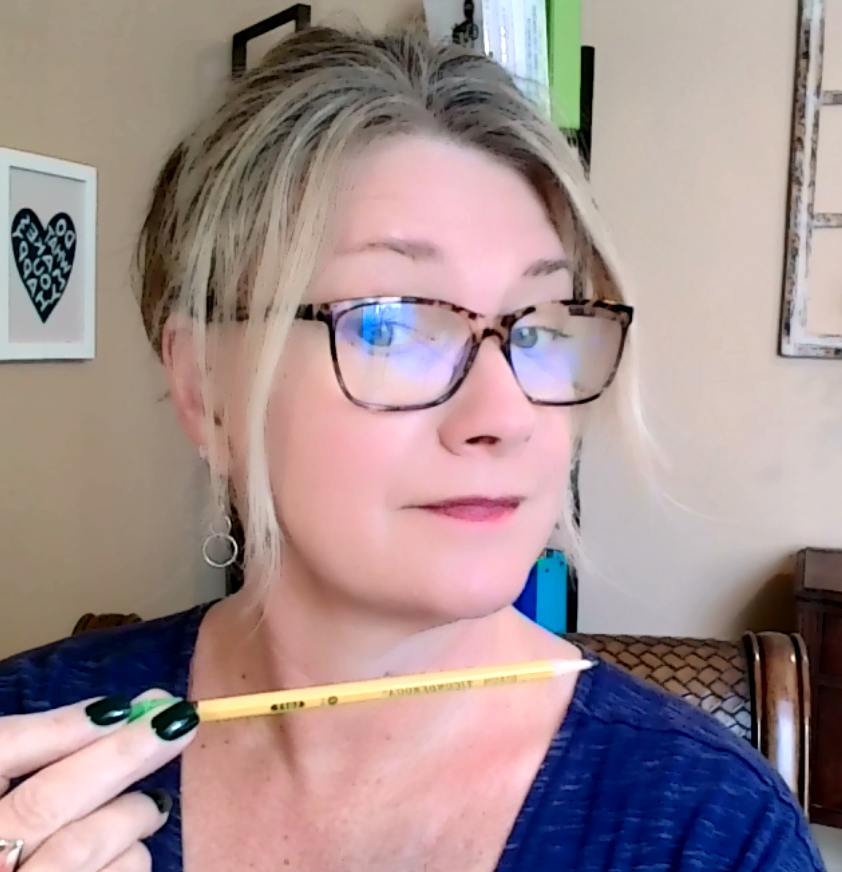 a blonde woman with brown glasses with hair up holding a yellow pencil