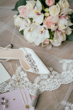 white high heel on top of a lace vail with a flower bouquet and invitation