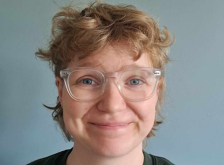 A woman with short blonde hair and glasses smiling at the camera, picture is of head and shoulders only.