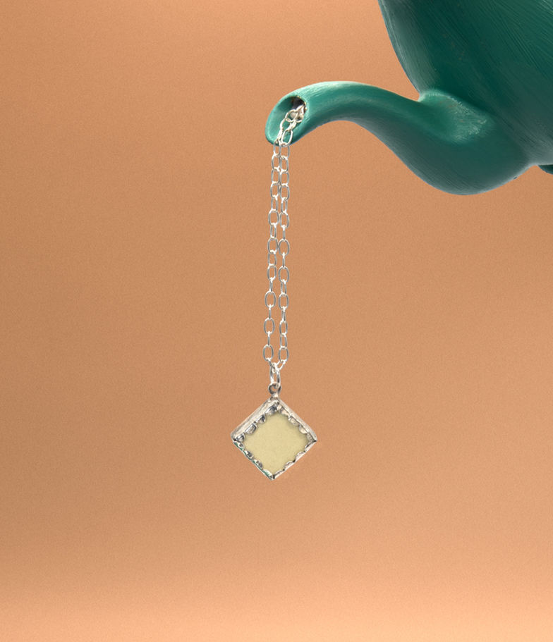 Silver necklace with pale yellow pendant hangs from teapot spout