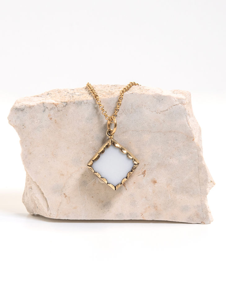 Gold necklace with white square pendant on rock