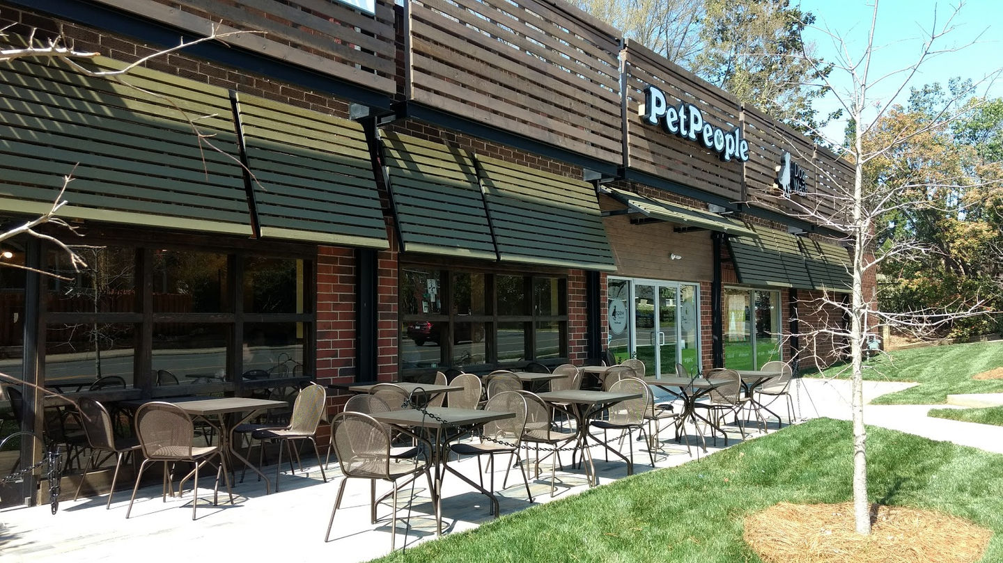 Outdoor patio seating area at Pet People after facade renovation in Charlotte, NC by Held Architecture, featuring green awnings, modern horizontal wood fins, brick cladding, and inviting outdoor furniture at The Courtyard shopping center in Dilworth.