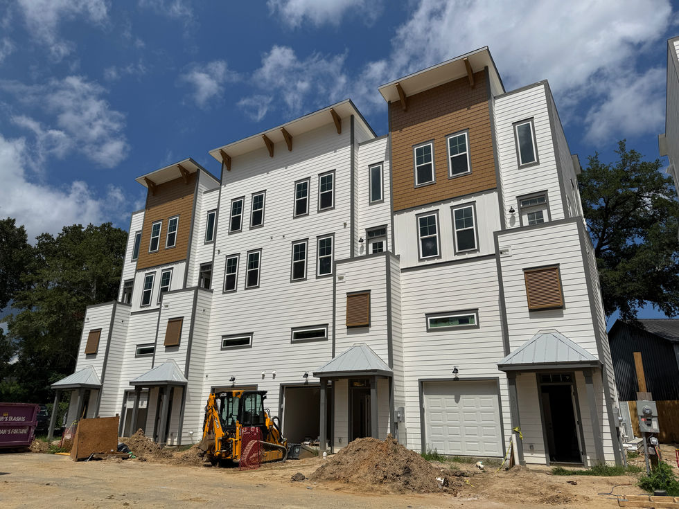 Modern townhomes under construction at Walk at Park Circle in North Charleston, SC, designed by Held Architecture. Featuring white horizontal siding, brown shingle accents, bold architectural forms, and an active construction site with dirt piles and utility equipment under a blue sky.