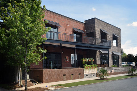 Exterior view of Nova’s Corner mixed-use building in Plaza Midwood, Charlotte, NC, designed by Held Architecture. Features red brick facade, second-floor terraces with black metal railings, black awnings, and modern commercial storefronts.