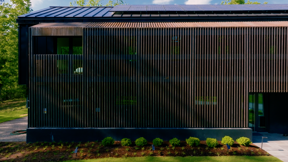 Close-up exterior detail of Nevills Creek Passive House showcasing dark vertical wood slat cladding, large windows, solar panels on the standing-seam metal roof, and modern design elements by Held Architecture in New Bern, North Carolina.