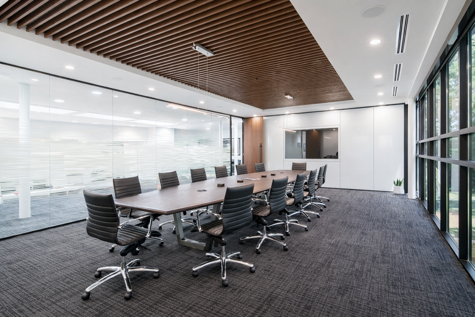Modern conference room at American Trützschler in Charlotte, NC after upfit by Held Architecture, featuring a large wood conference table, black leather executive chairs, wood slat ceiling, frosted glass walls, and abundant natural light from large windows.