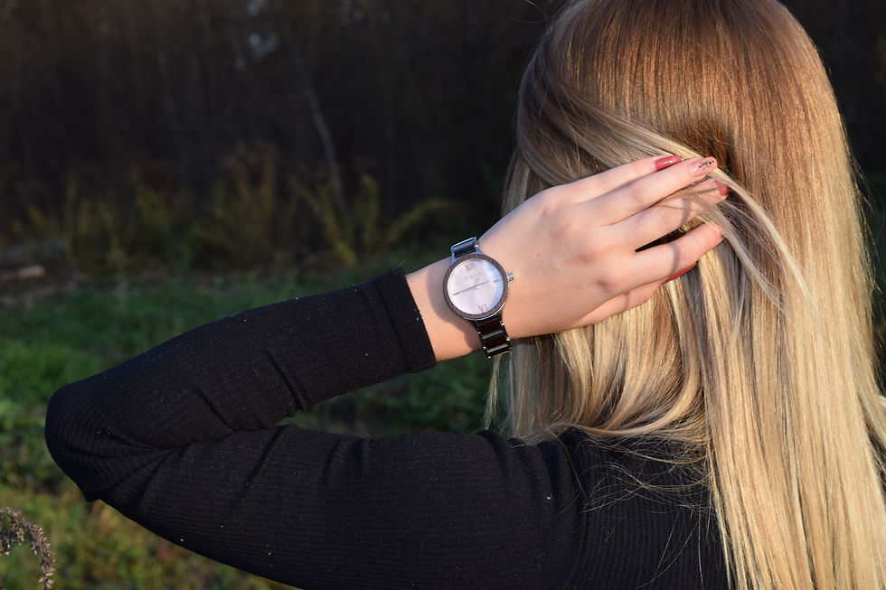 Eine Frau von hinten fotografiert, fasst sich mit einer Holzherz Holzuhr in die Haare