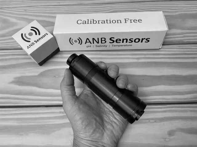 An ANB Sensors calibration-free pH sensor held in a hand, with its packaging behind.