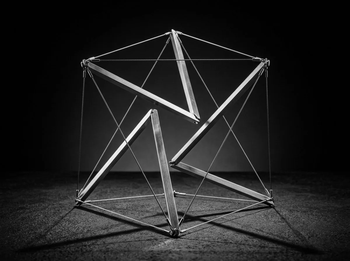 A tensegrity sculpture: steel struts held in balance by taut cables, none touching.