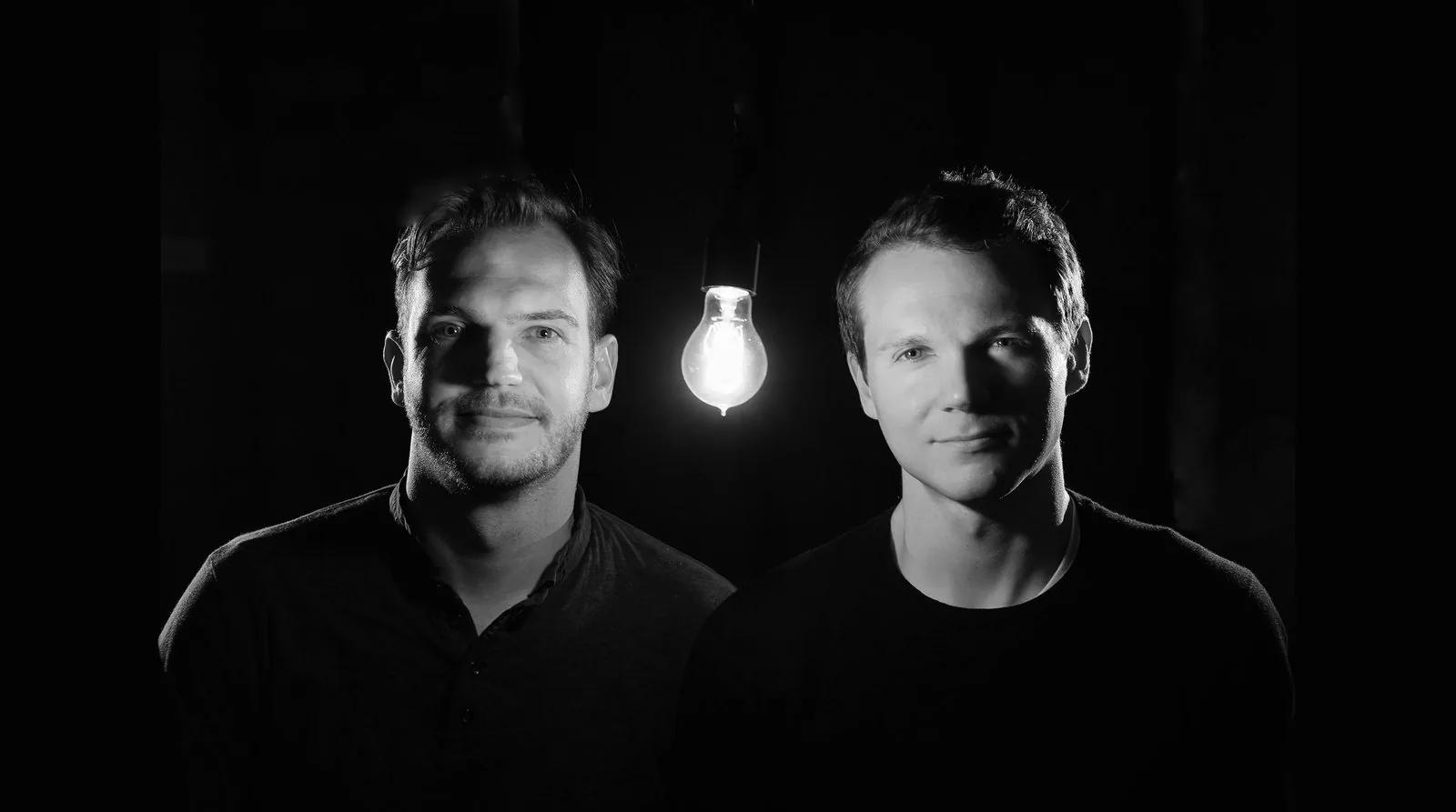 Two members of the NearSt team beside a single hanging light bulb.