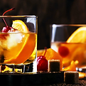 Two Old Fashioned cocktails sit on a table separated by a cherry