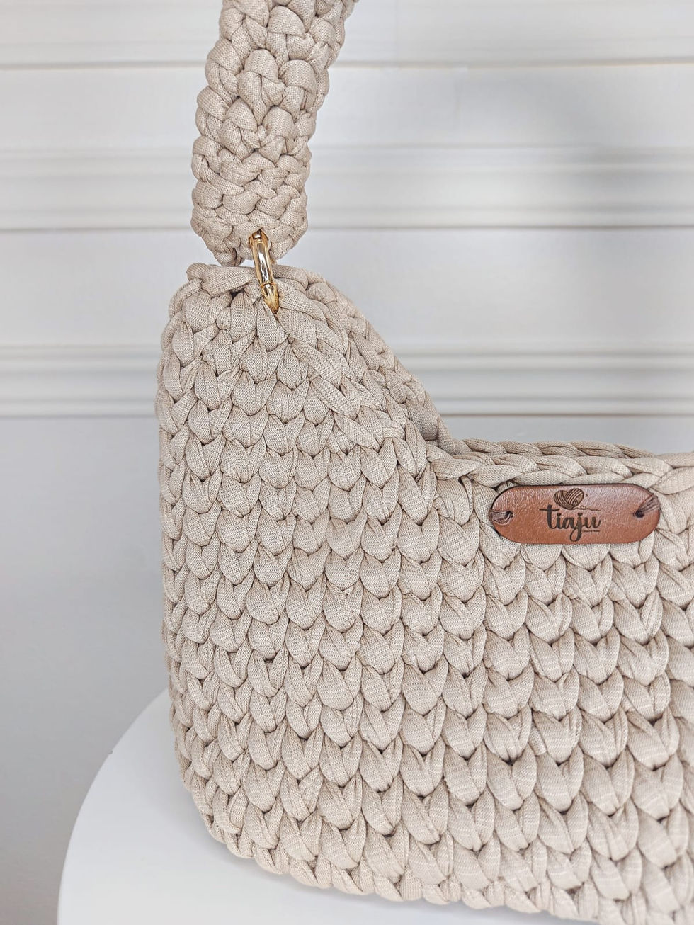 Bolsa em crochê com fio de malha bege, alça também em crochê, detalhe em tassel com acabamento dourado.