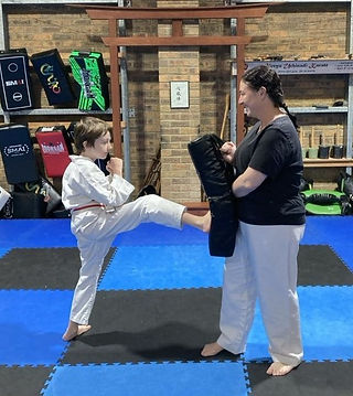 Student practicing front kick into pad held by mum