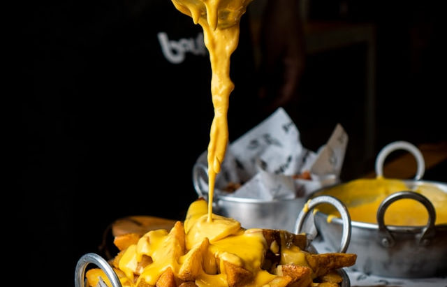 Joppie saus wordt over friet in een metalen pan gegoten, een recept voor een gele en koude saus.