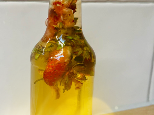 Fles met aardbeien in azijn, gemaakt van restjes aardbei en rode dop op houten tafel, tegen witte muur, met fel licht.