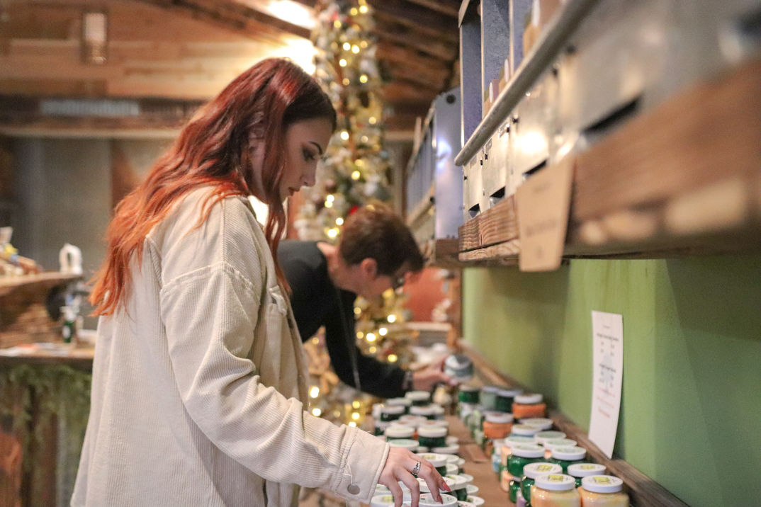 Two women smell various soaps, facial scrubs, and other all-natural handmade products.