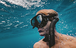 Man snorkeling underwater surrounded by bubbles in clear blue ocean.