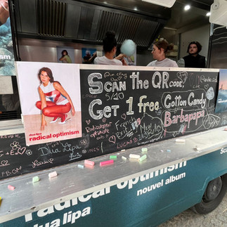 A food truck decorated in the colours of Dua Lipa's album, with cotton candy being handed out.