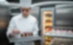 Vignette photoréaliste d’une cuisine centrale moderne : chef en tenue hygiénique déposant un dessert premium surgelé sur plateau gastronorme, chariot réfrigéré avec vapeur froide et porte de chambre froide en arrière-plan, chaîne du froid maîtrisée – Les Saveurs de René