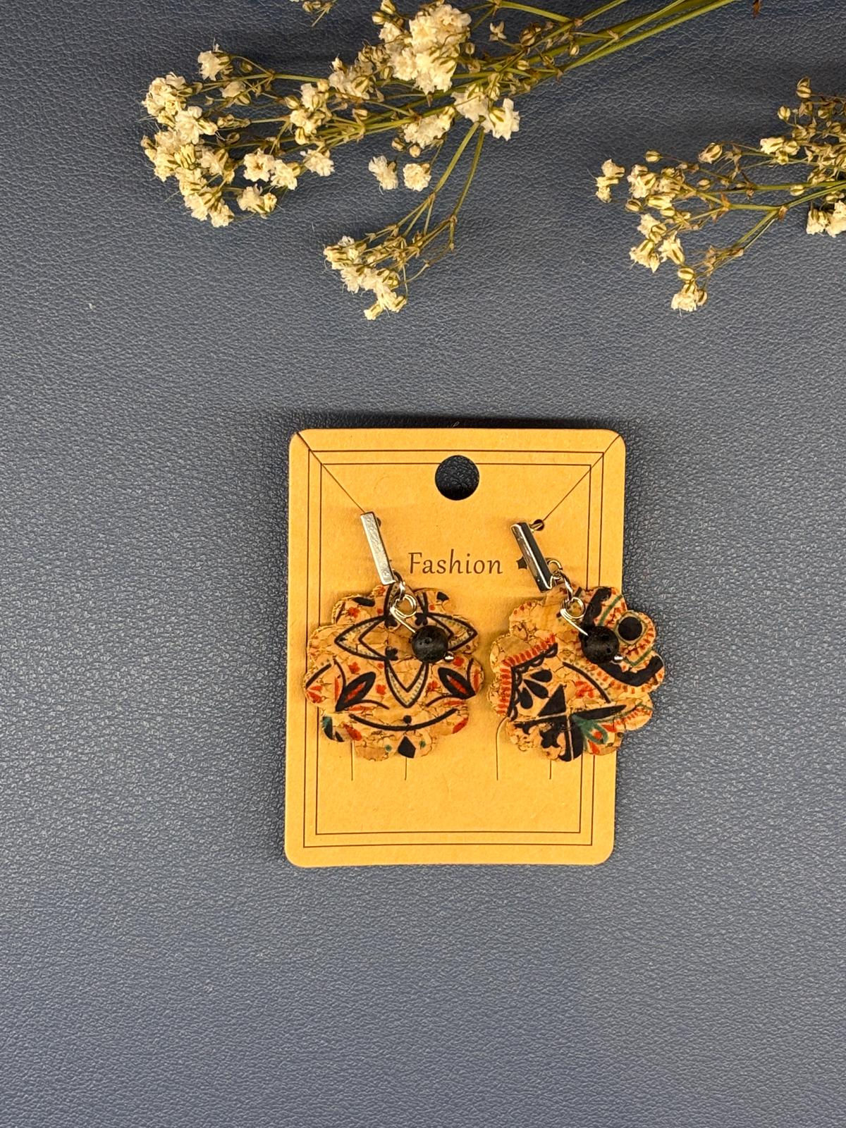 Boucles d'oreilles pendantes à motifs noirs et orange sur carte brune.
