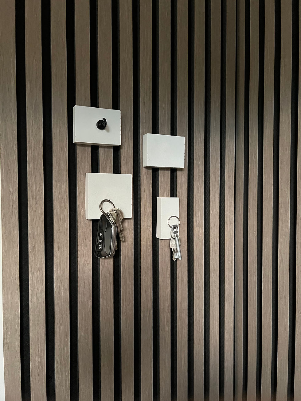 Stilvolle Wandorganisation mit weißen Magnetblöcken auf einer Holzlwand, an denen mehrere Schlüssel sicher befestigt sind