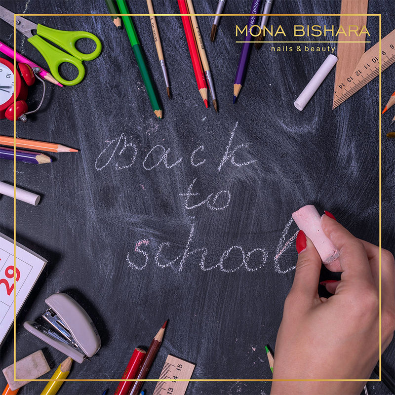 Hand writes back to school on a chalkboard with school supplies