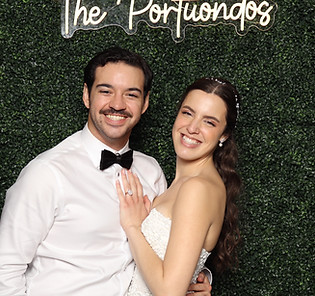 Couple smiling at a glam photo booth with hedge wall.
