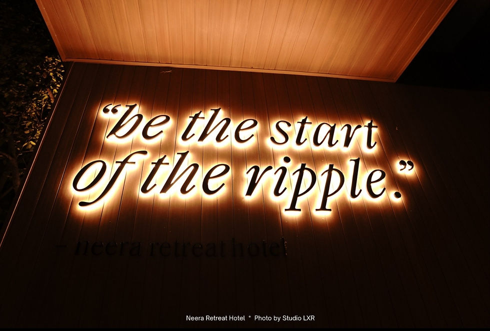 Illuminated quote "be the start of the ripple" on a wooden wall, glowing warmly. Neera Retreat Hotel text below, creating an inspiring mood.