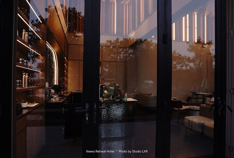 Modern interior with large glass doors, cozy seating, and warm lighting. Reflections of trees outside add a serene ambiance.