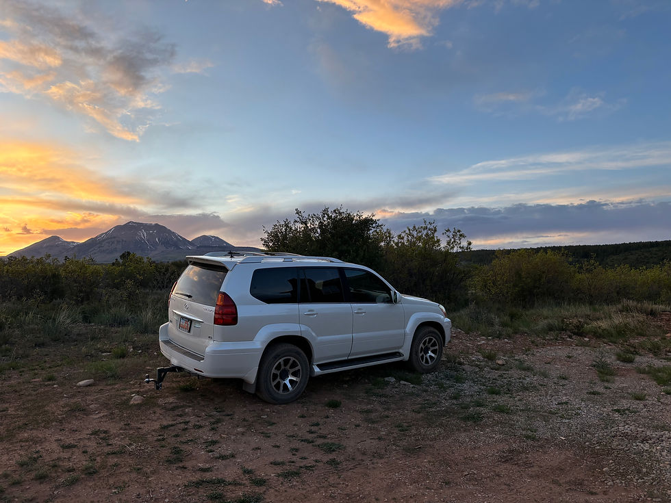 A white SUV in the desert with the mountains and the sunset in the background.
