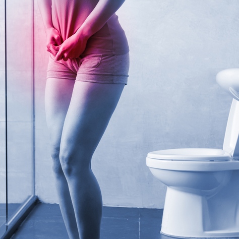 Mulher com dor na região pélvica em frente ao vaso sanitário, representando sintomas de infecção urinária (ITU) e desequilíbrio do microbioma urinário.