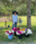 Eight Gates Farm owner Barbara McFadyen wearing a navy blue sun hat and standing behind buckets of colorful flowers